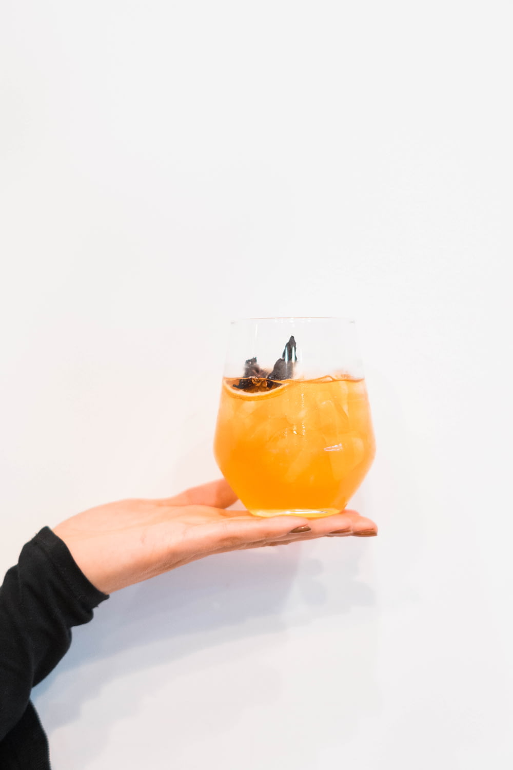 person holding clear drinking glass with orange liquid