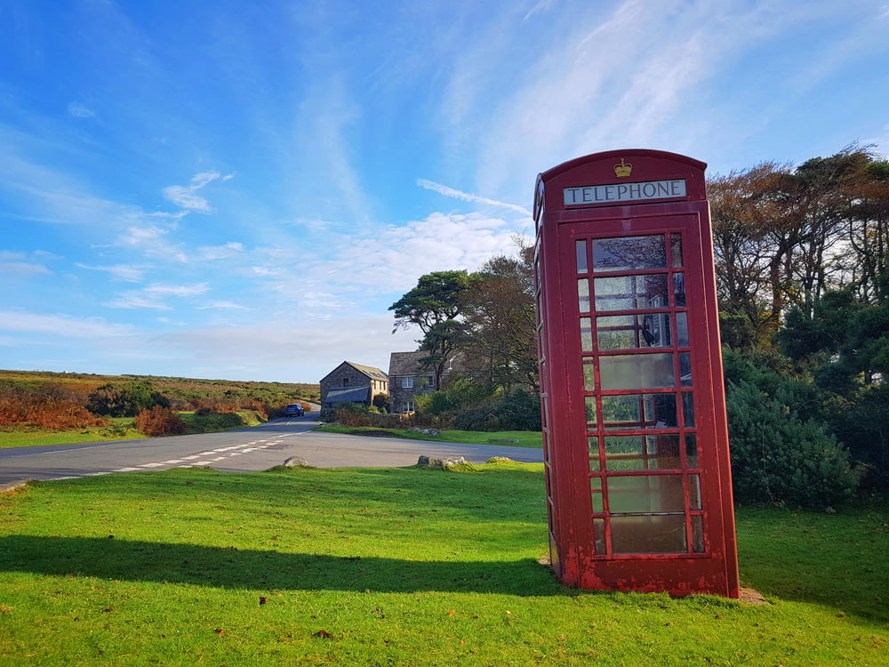 red telephone booth on green grass field under blue sky during daytime