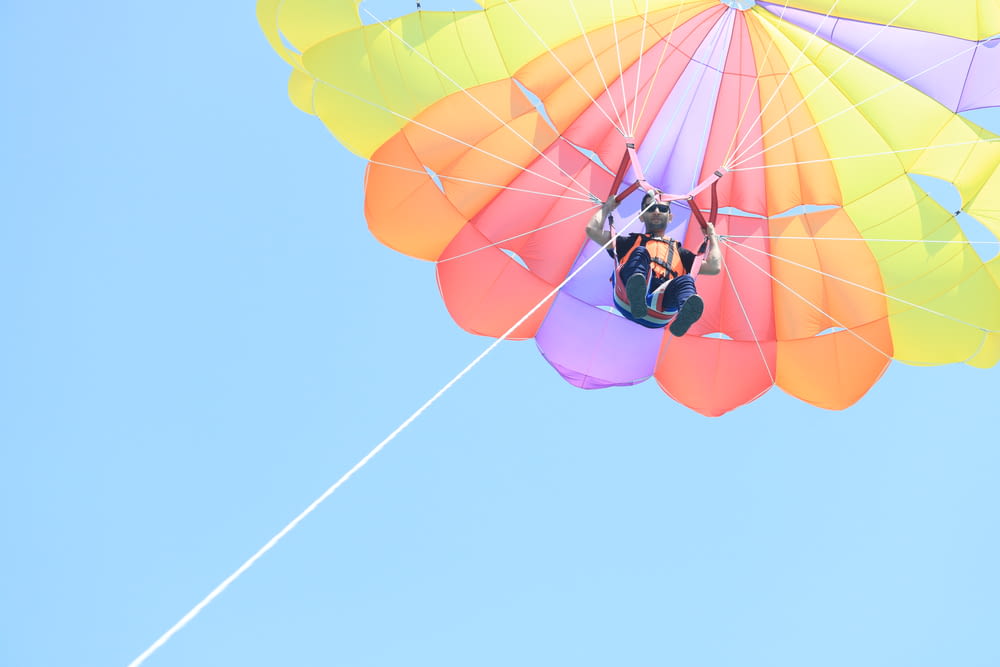 man in black jacket and blue pants riding yellow and red parachute