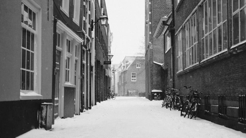 grayscale photo of snow covered road between buildings