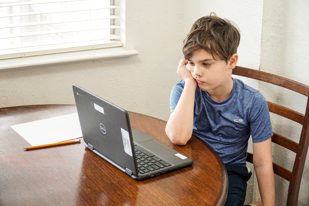 T-shirt del ragazzo in girocollo blu con MacBook Pro sul tavolo di legno marrone