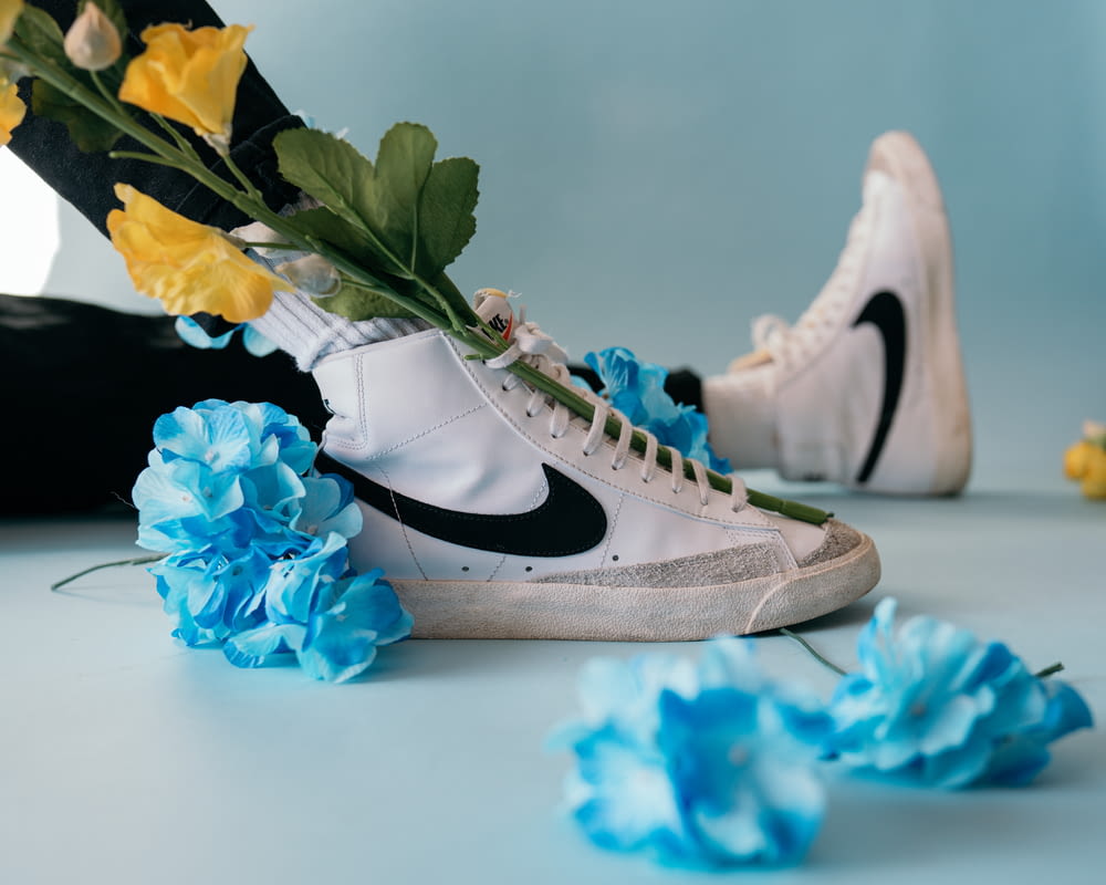 white and black nike sneakers beside blue flowers