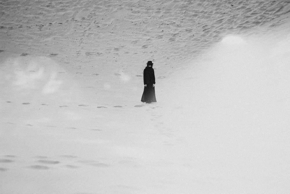 person in black coat walking on snow covered field during daytime