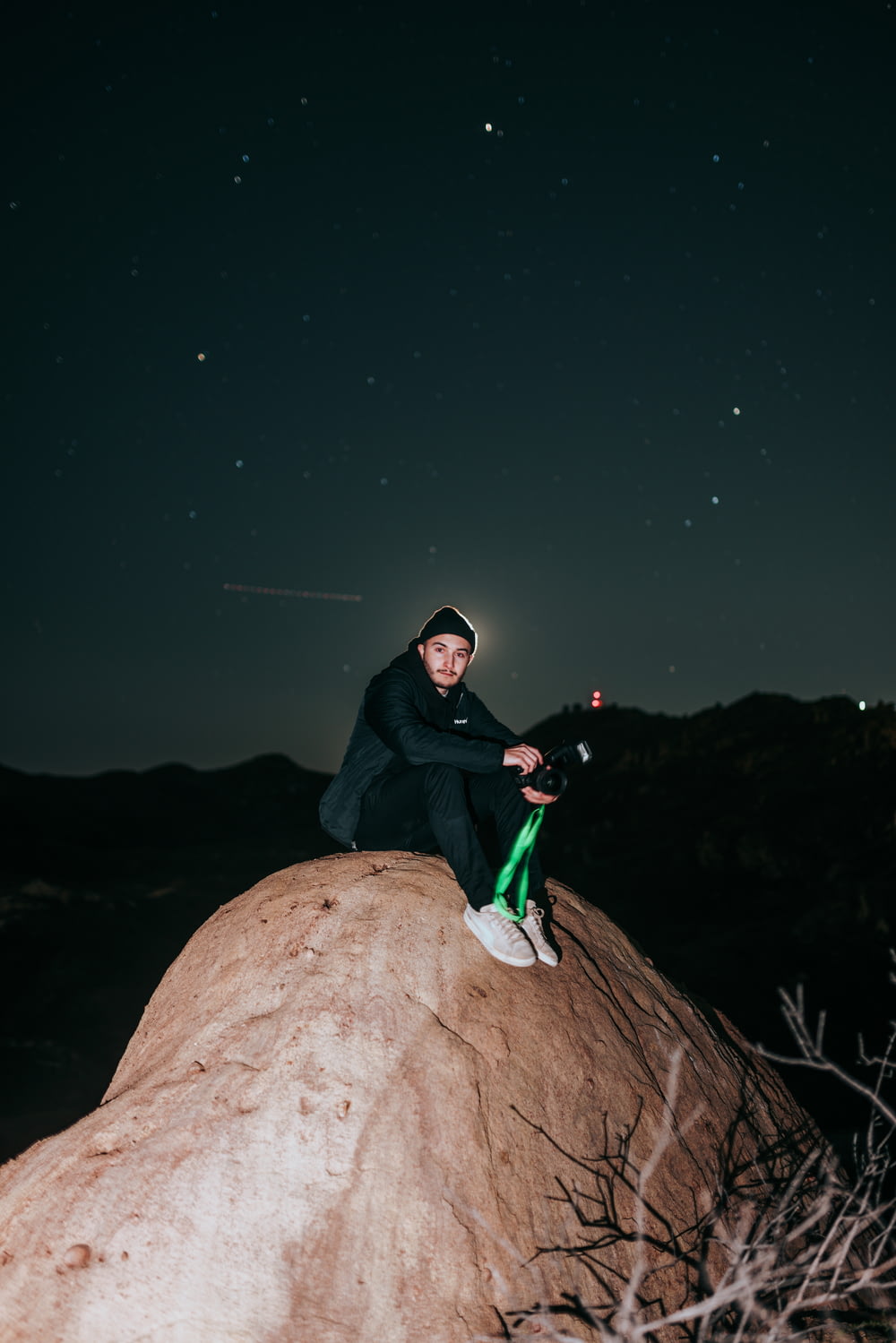 man in black jacket and green pants sitting on brown rock during night time