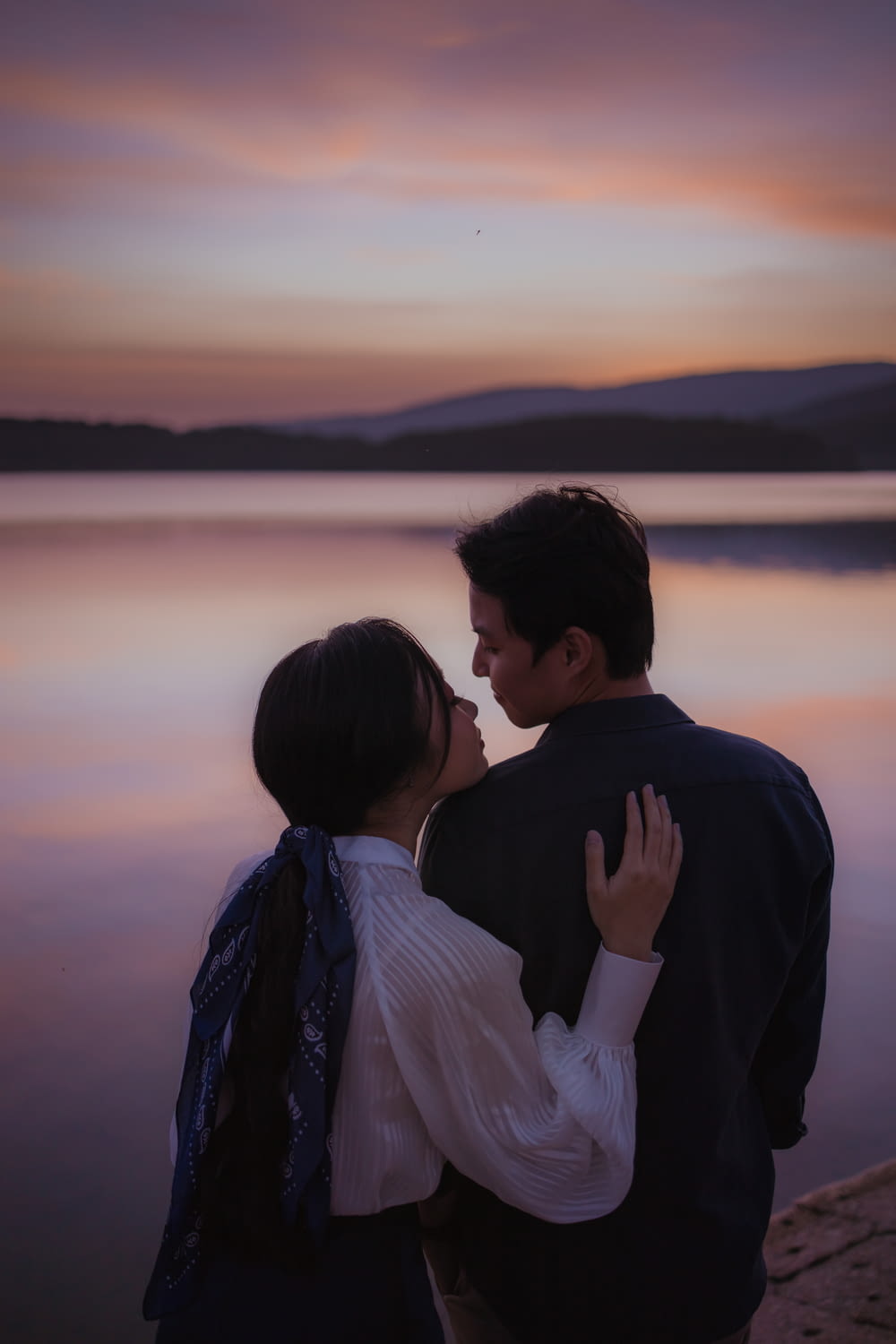 man and woman standing near body of water during sunset