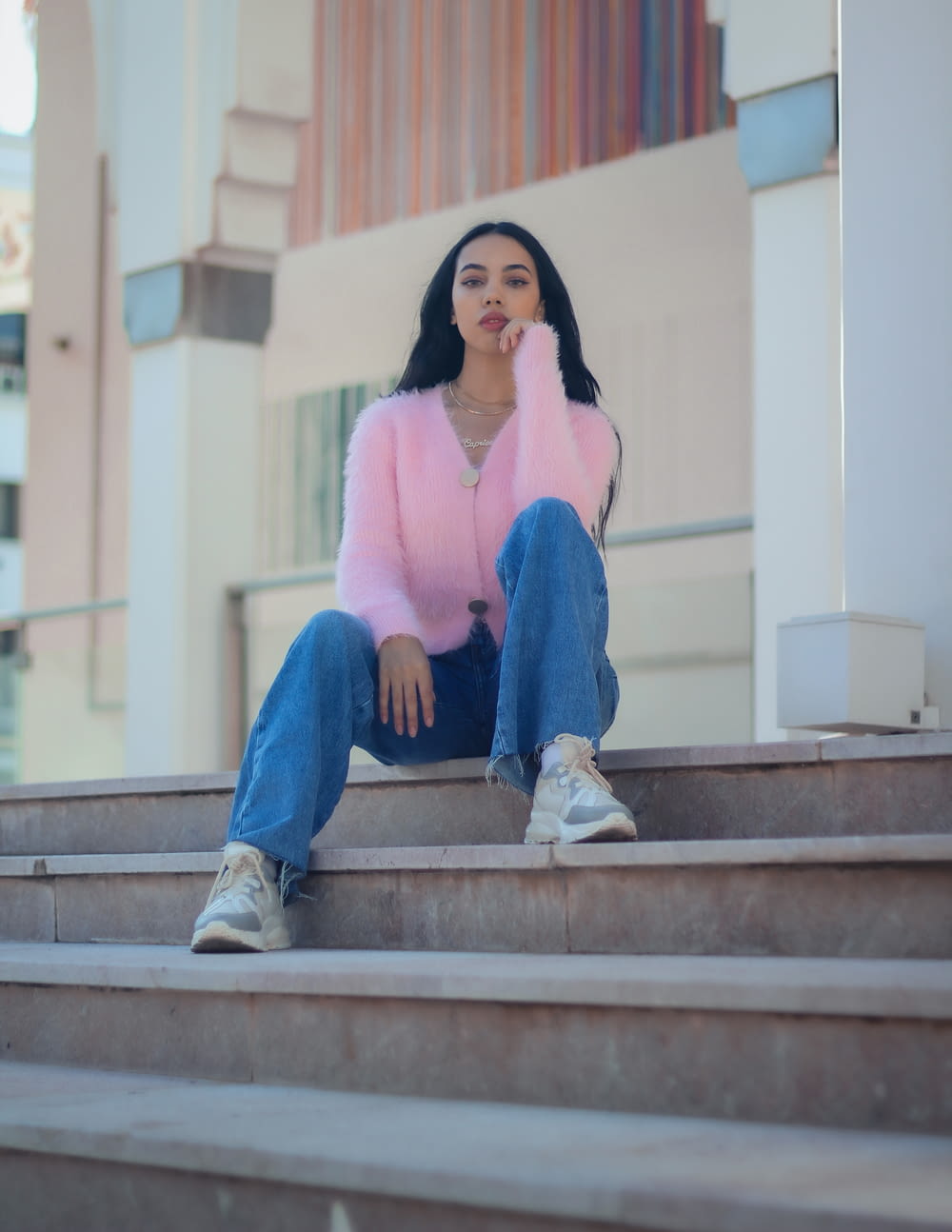 woman in pink long sleeve shirt and blue denim jeans sitting on brown concrete stairs