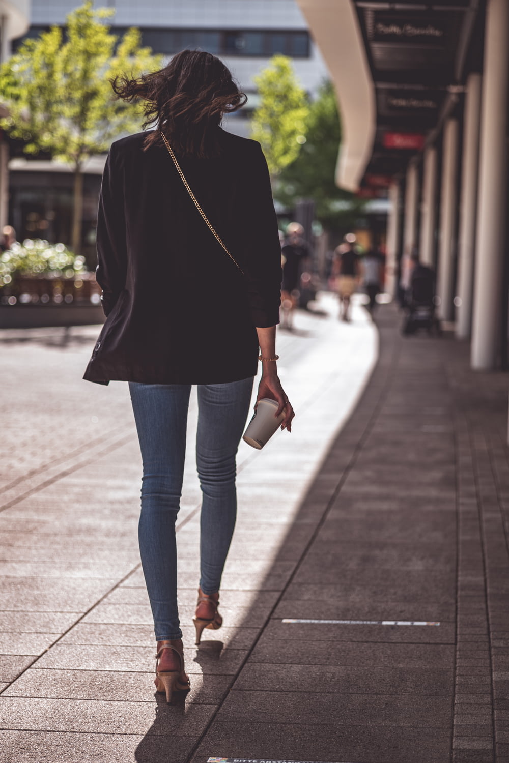 woman in black long sleeve shirt and blue denim jeans walking on sidewalk during daytime