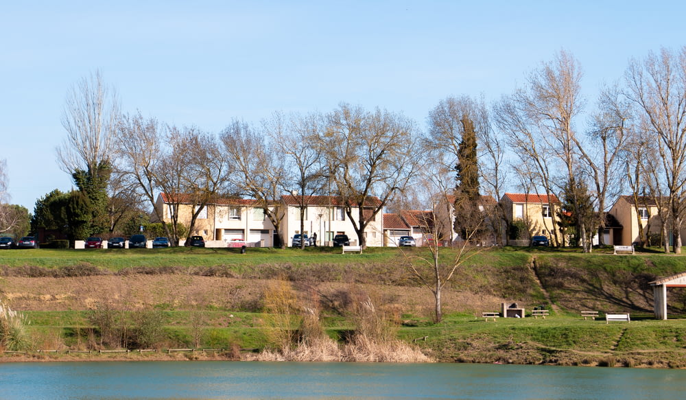 white and brown house near green trees and body of water during daytime