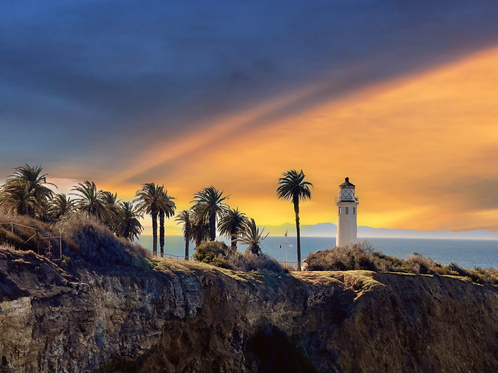 white lighthouse near palm trees during sunset