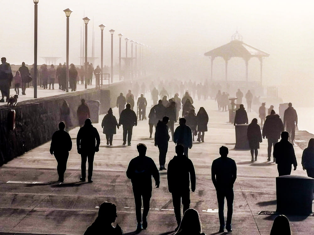 silhouette de personnes marchant sur un trottoir en béton gris pendant la journée