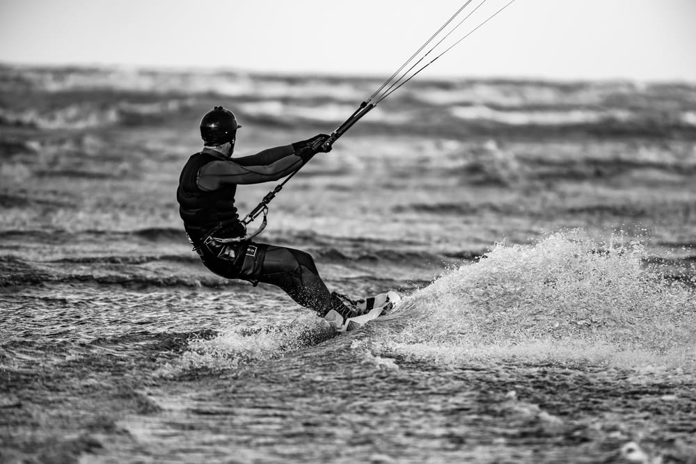 uomo in giacca nera e pantaloni neri che gioca a fare windsurf sulle onde del mare