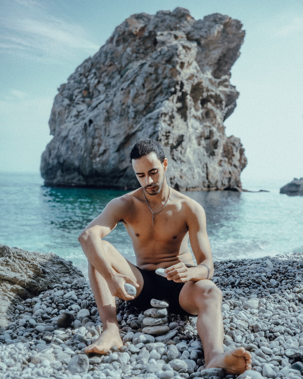 topless man sitting on rock near body of water during daytime
