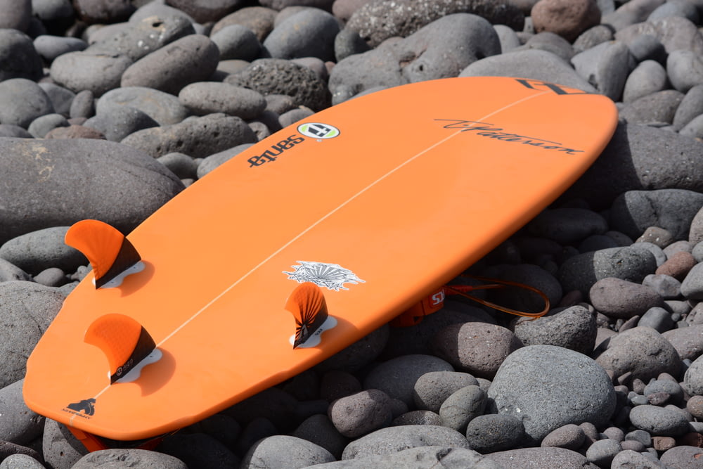 orange surfboard on gray stones
