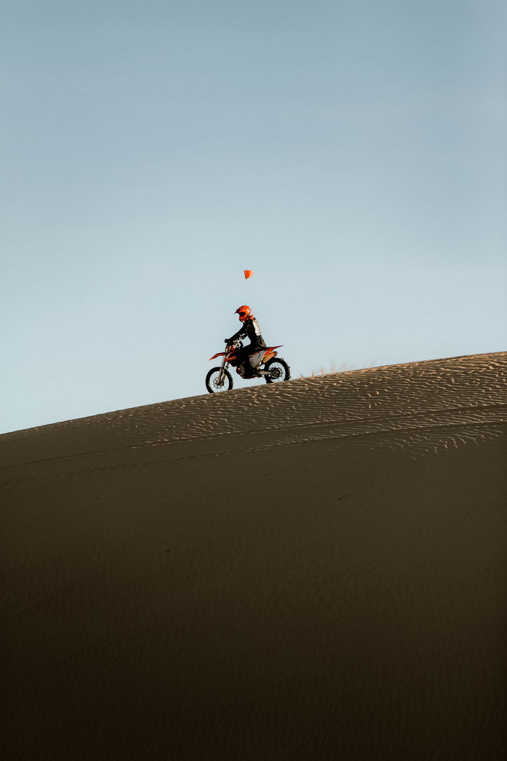 uomo in camicia rossa che guida la motocicletta sulla sabbia marrone durante il giorno