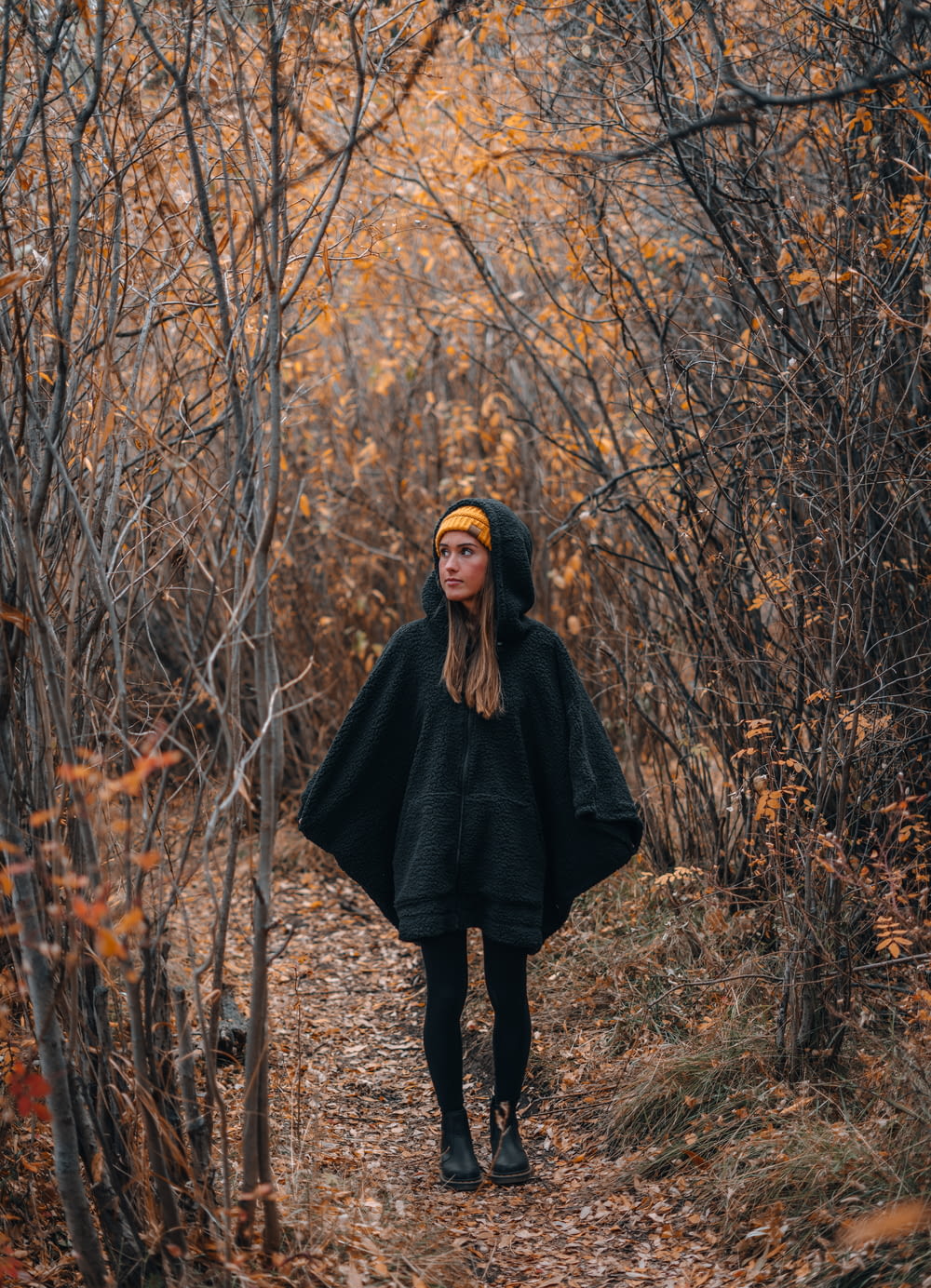 낮 동안 갈색 잔디밭에 서 있는 검은 코트를 입은 여자