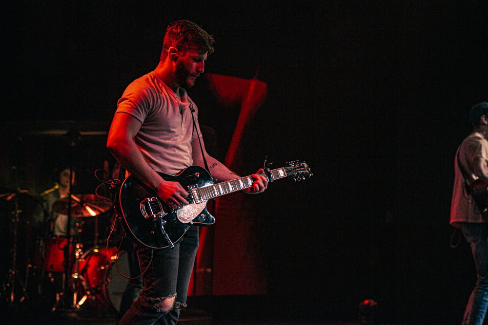 uomo in t-shirt girocollo nera che suona la chitarra elettrica