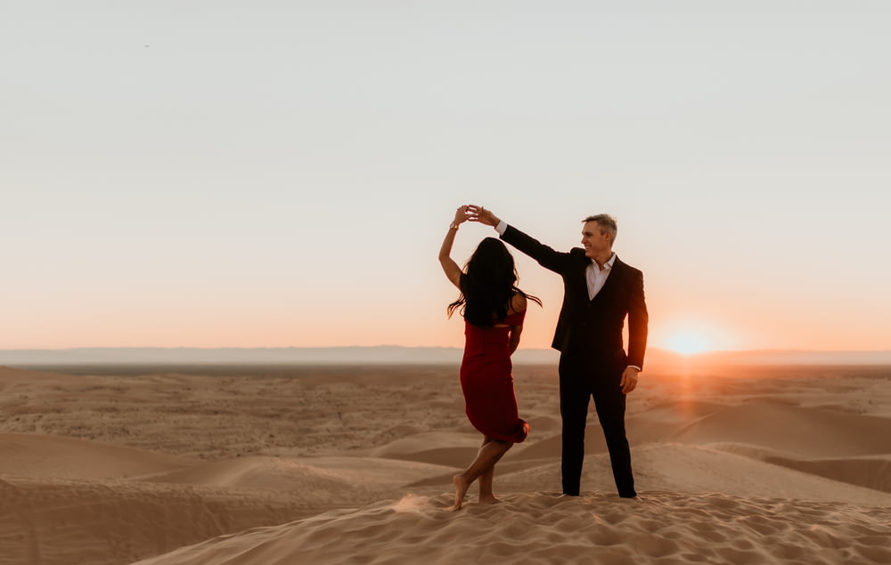 man and woman standing on brown sand during sunset