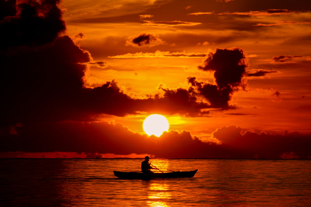 silhouette of man riding on boat during sunset
