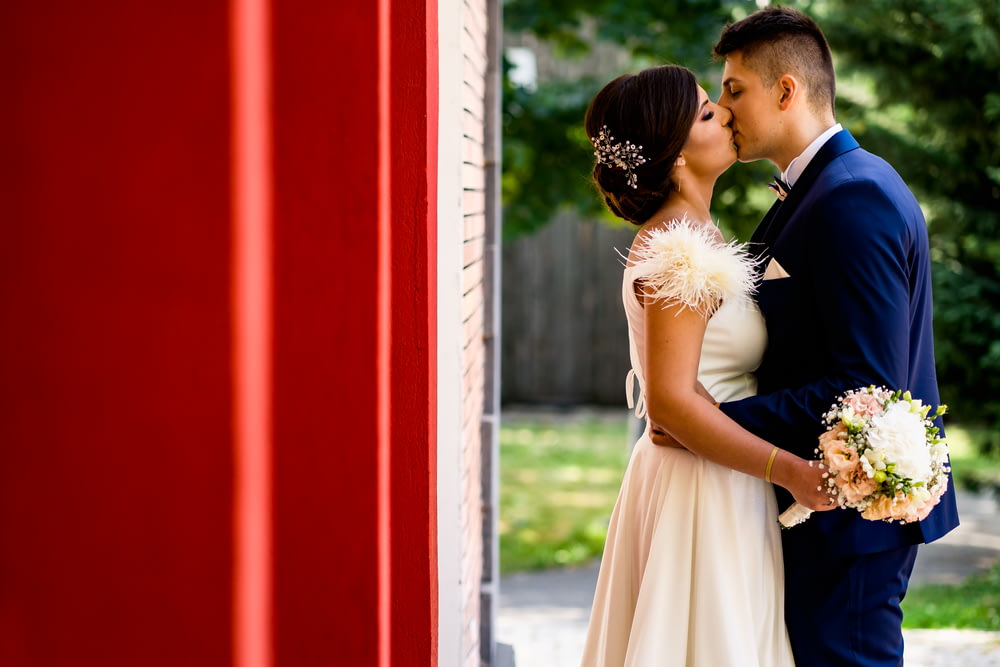 man and woman kissing near red wall during daytime