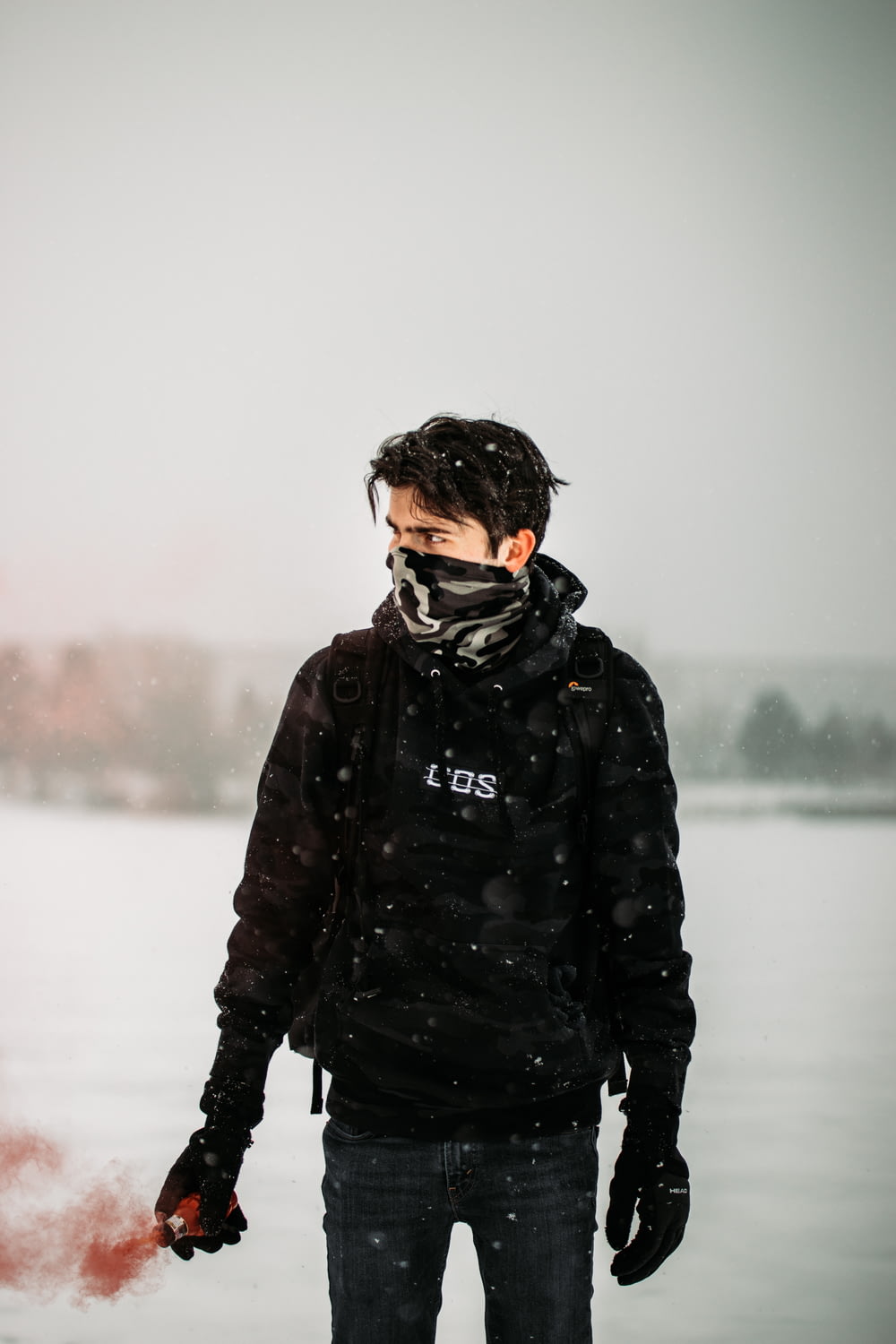 Hombre con chaqueta negra y mochila negra de pie en suelo cubierto de nieve