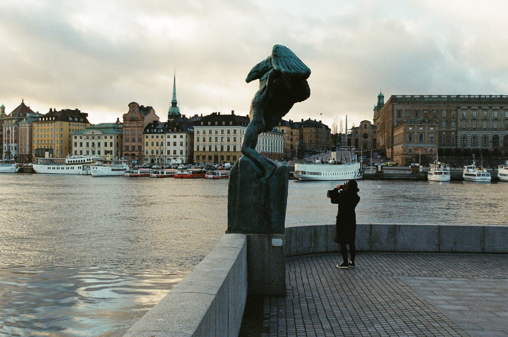 statue of man holding umbrella near body of water during daytime