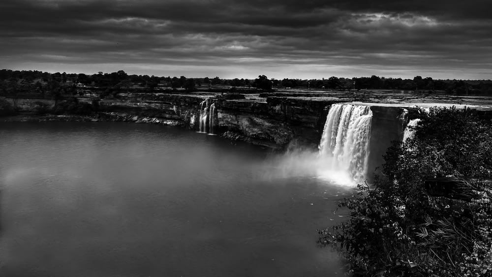 grayscale photo of waterfalls under cloudy sky