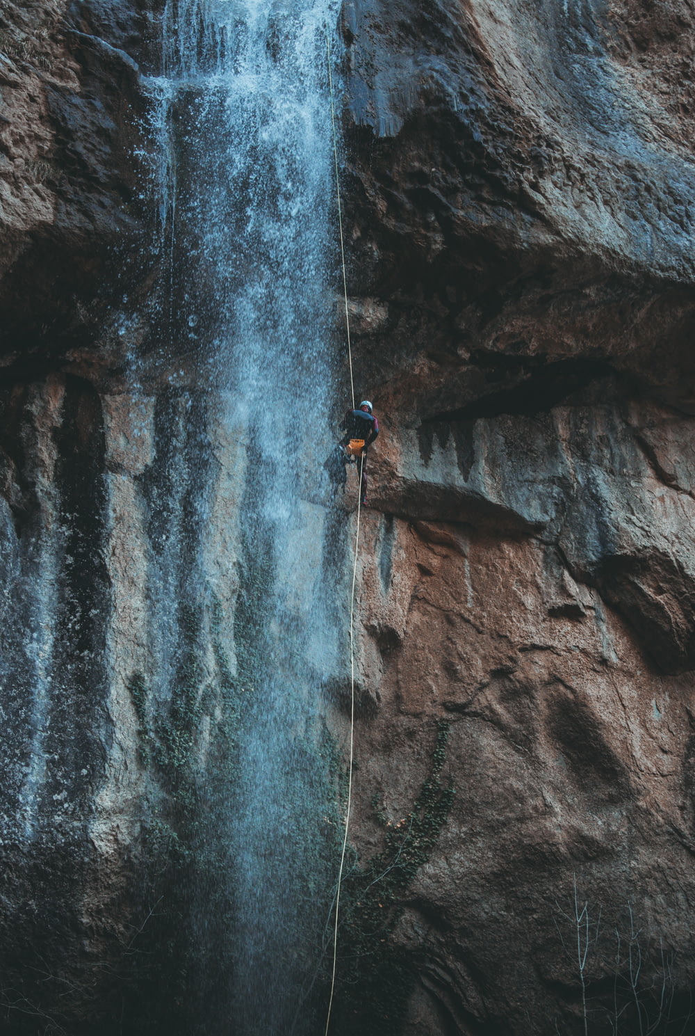 pessoa na jaqueta azul escalando na montanha rochosa durante o dia