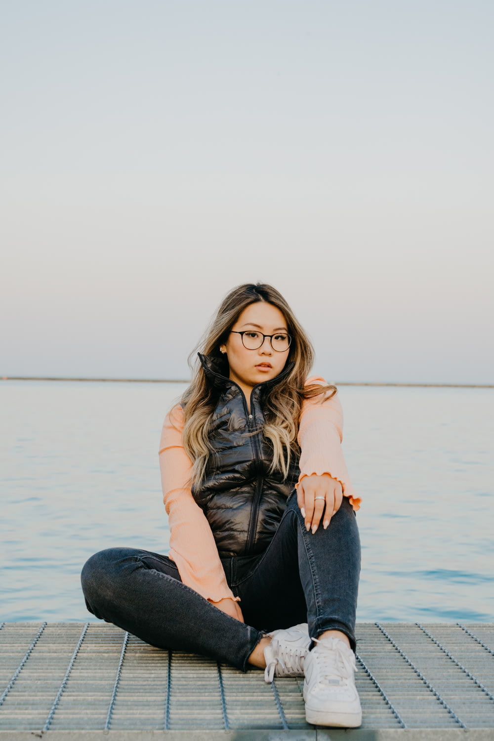 woman in brown shirt and blue denim jeans sitting on rock near body of water during
