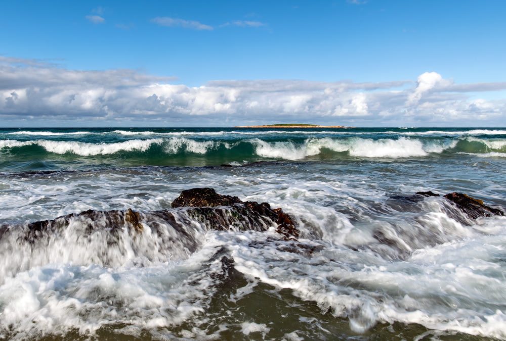 ocean waves crashing on shore under blue sky during daytime