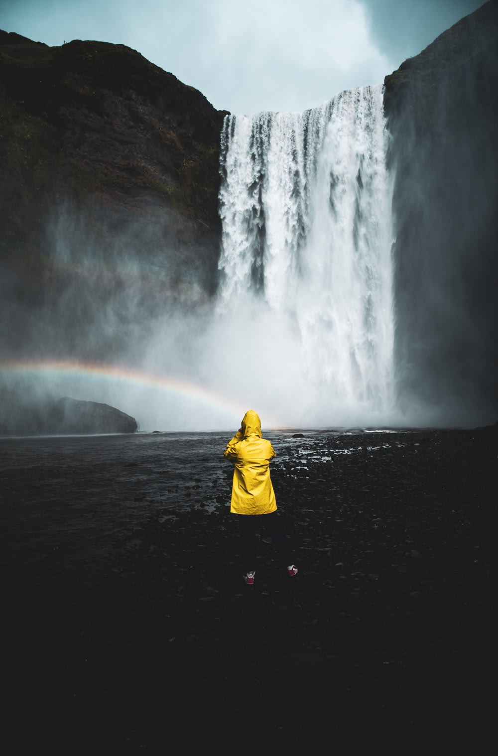 pessoa em moletom amarelo em pé na frente de cachoeiras