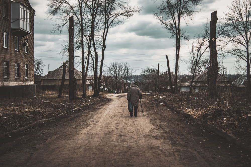 man in gray jacket walking on dirt road during daytime