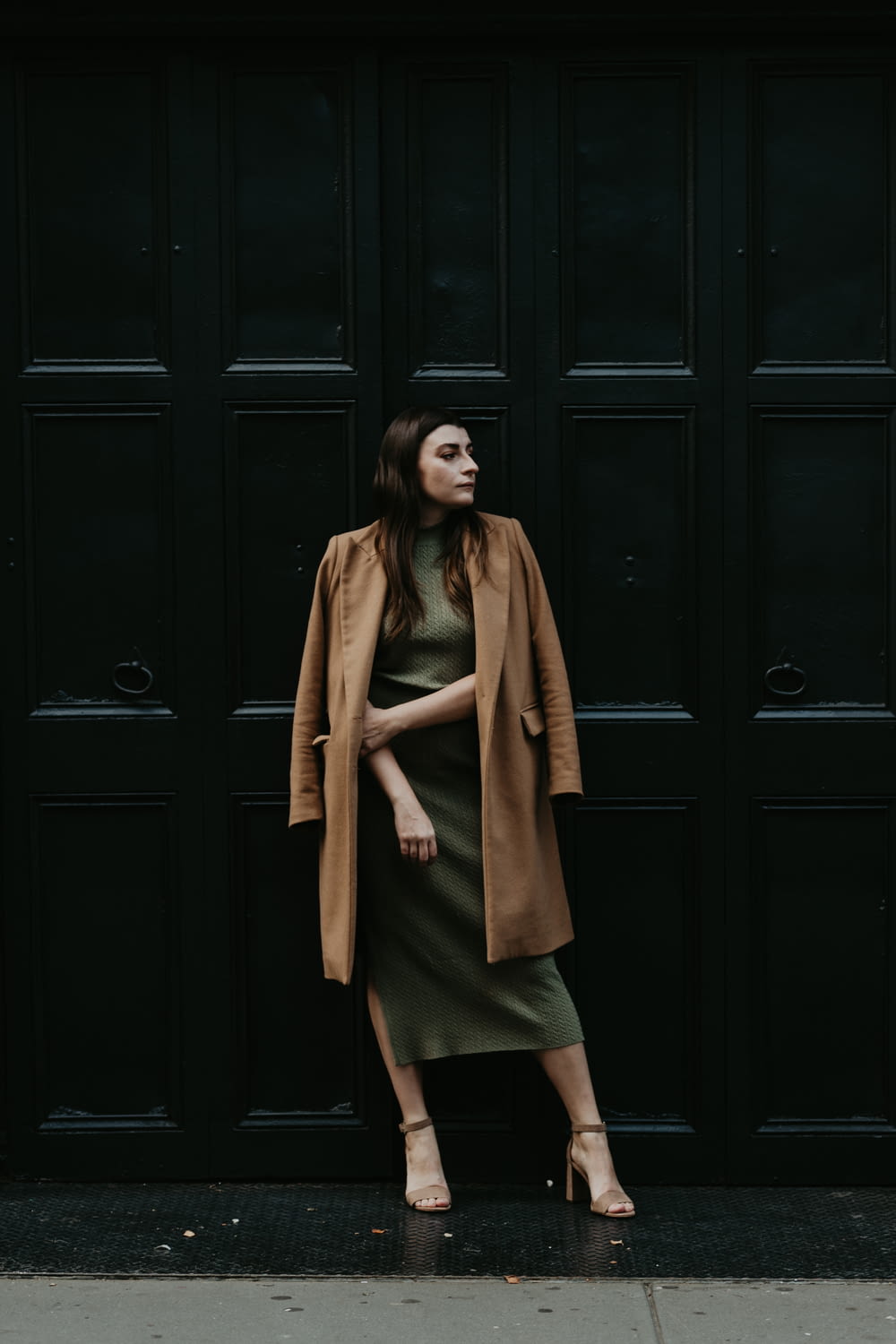 woman in brown coat standing beside black wooden door