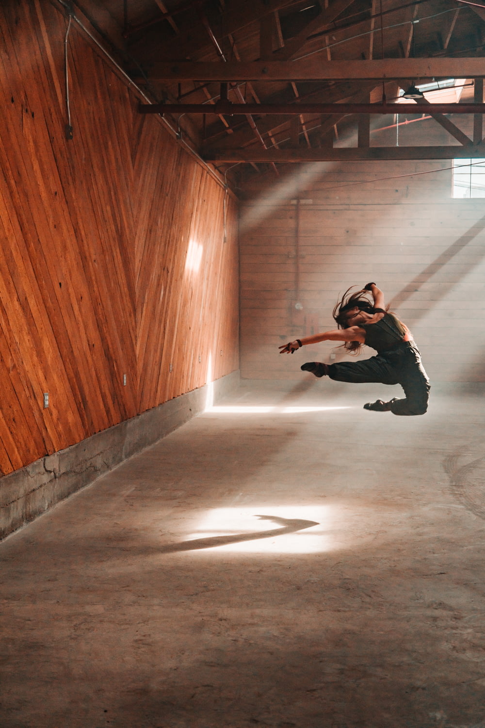 man in black jacket and black pants jumping on brown wooden floor
