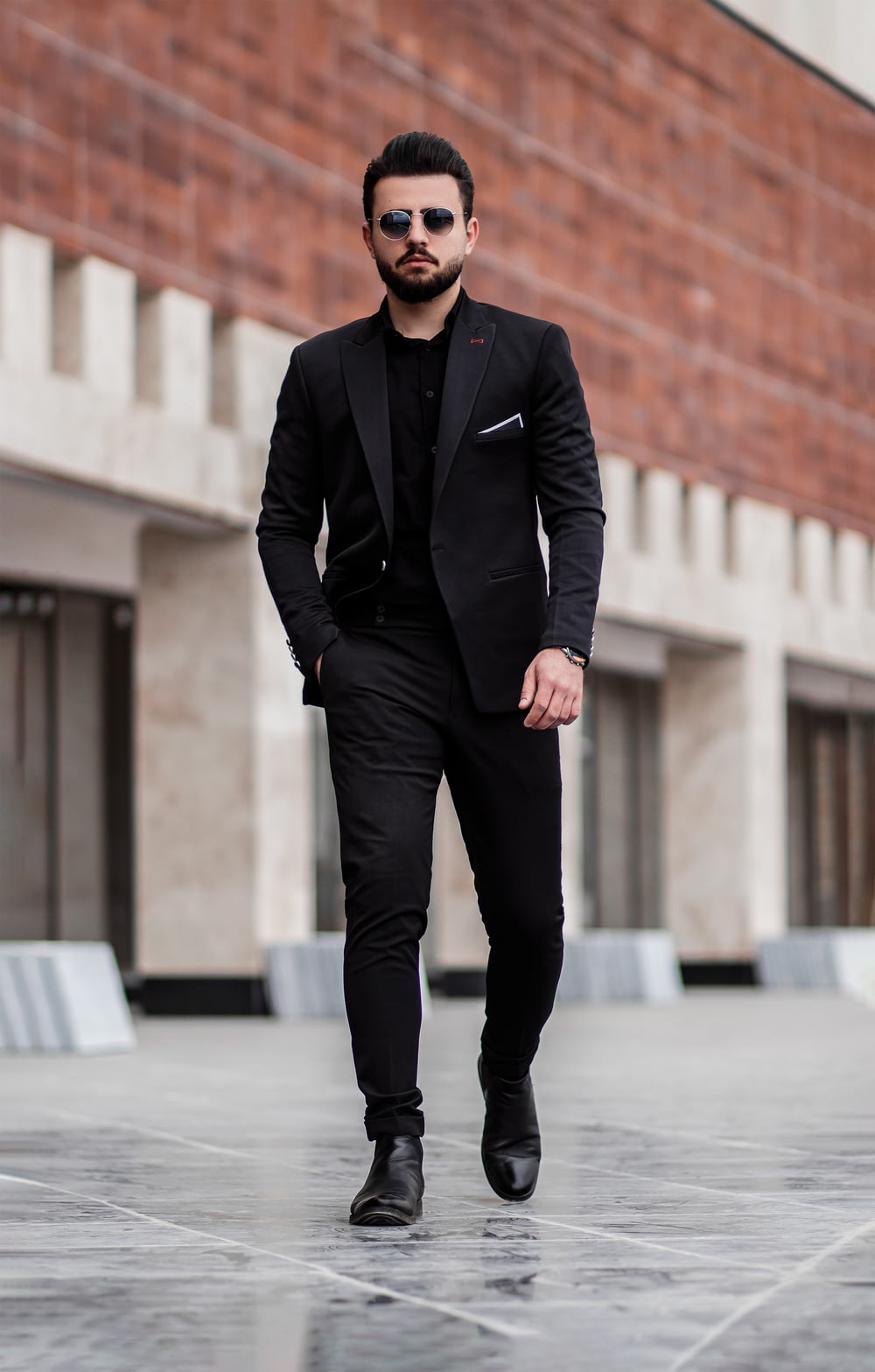 昼間、灰色のコンクリートの床に立つ黒いスーツのジャケットと黒いズボンを着た男