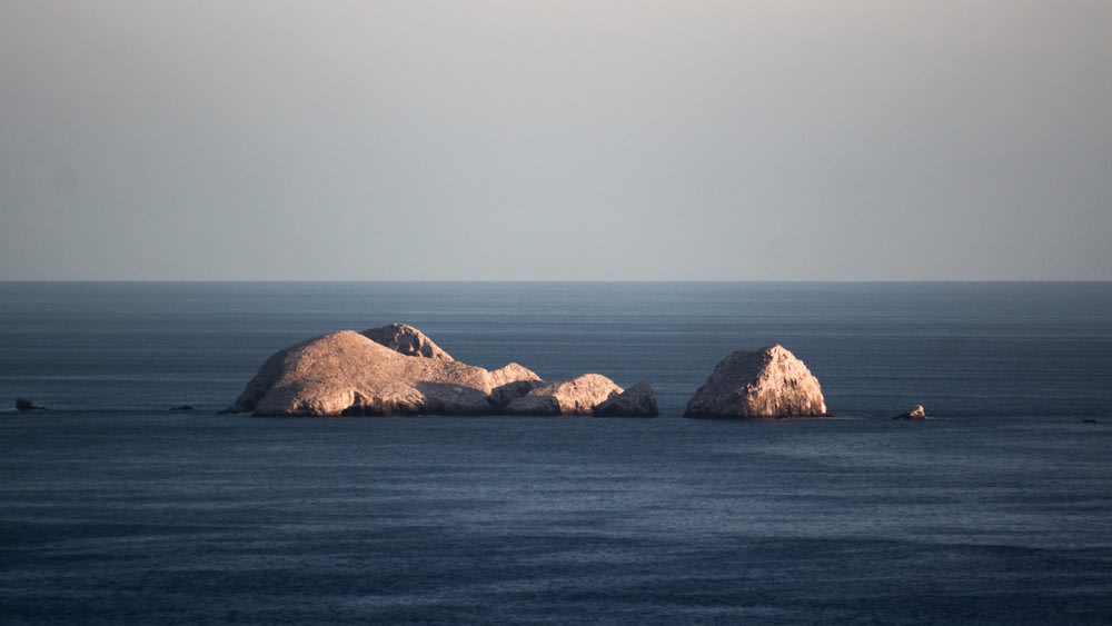 formação rochosa marrom no mar azul sob o céu branco durante o dia