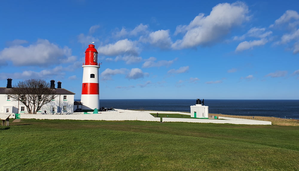 white and red lighthouse near body of water under blue sky during daytime