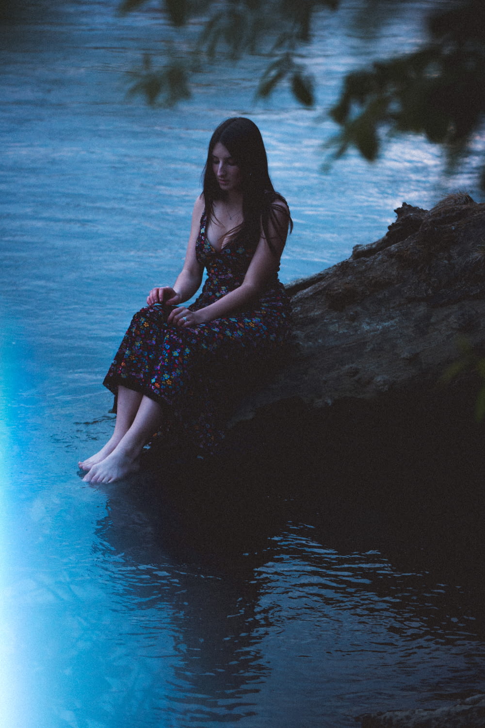 woman in black and red floral dress sitting on rock near body of water during daytime