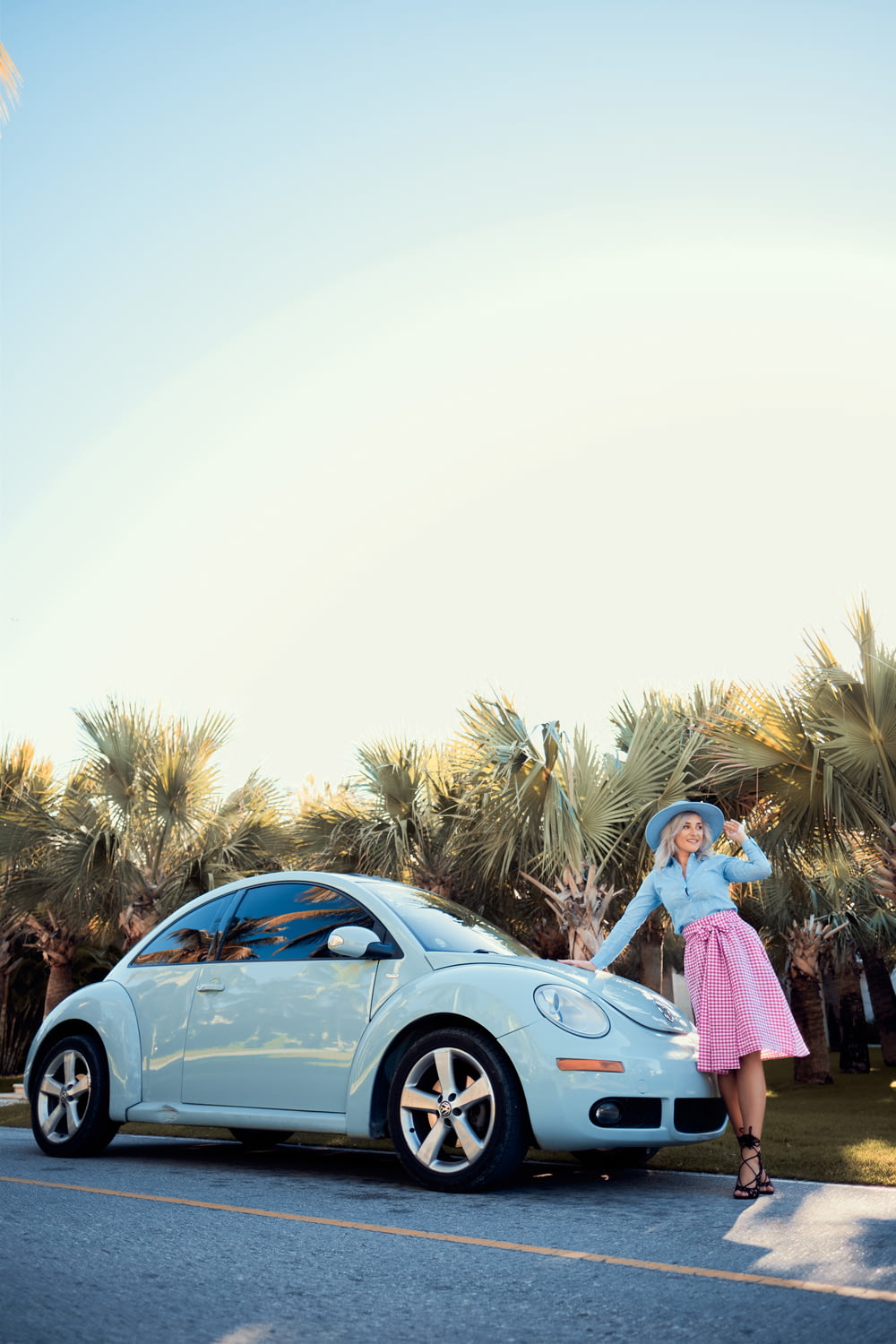 woman in pink dress standing beside blue car during daytime