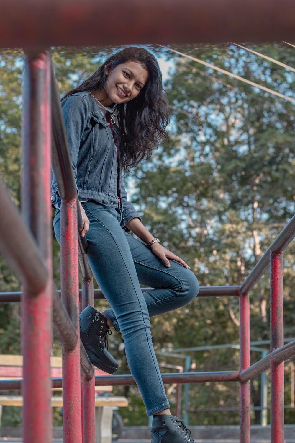 woman in blue denim jeans sitting on red metal railings during daytime