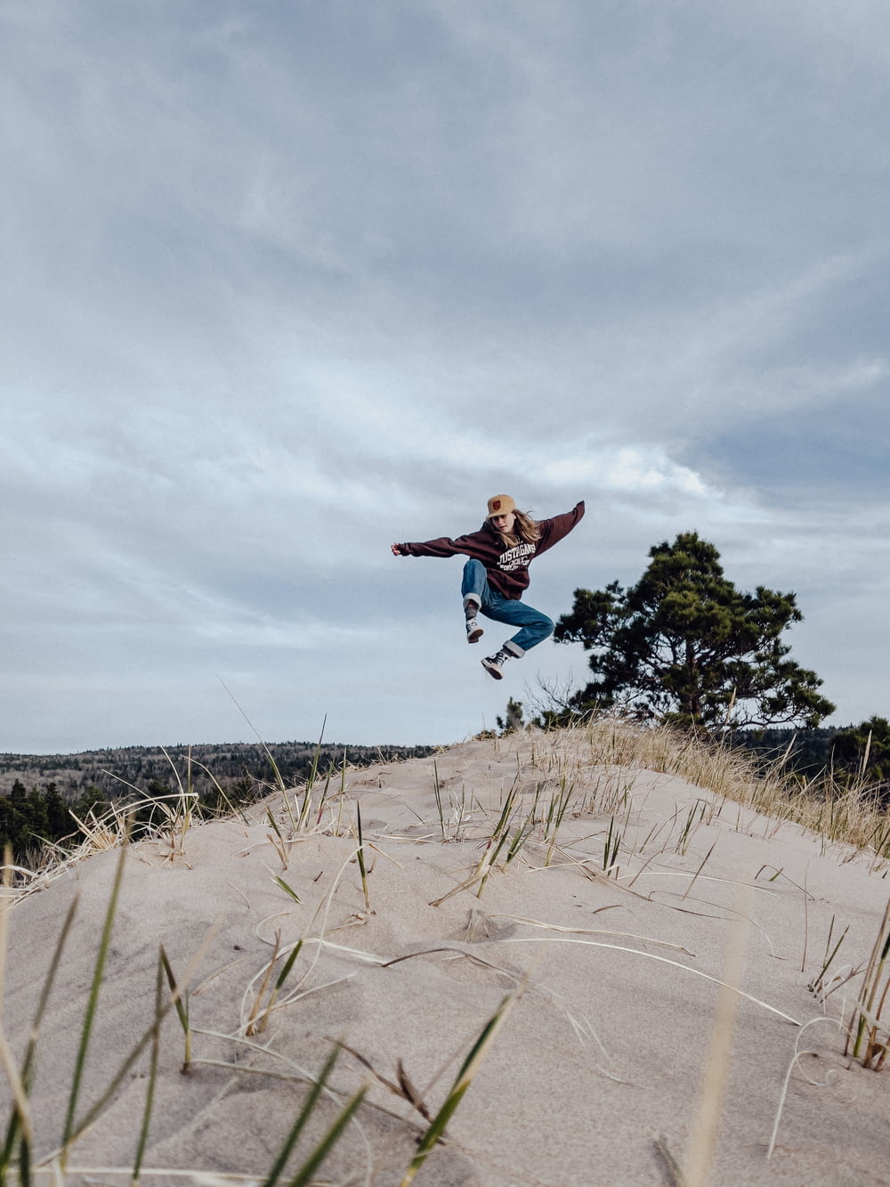 man in blue jacket and blue denim jeans jumping on brown sand during daytime