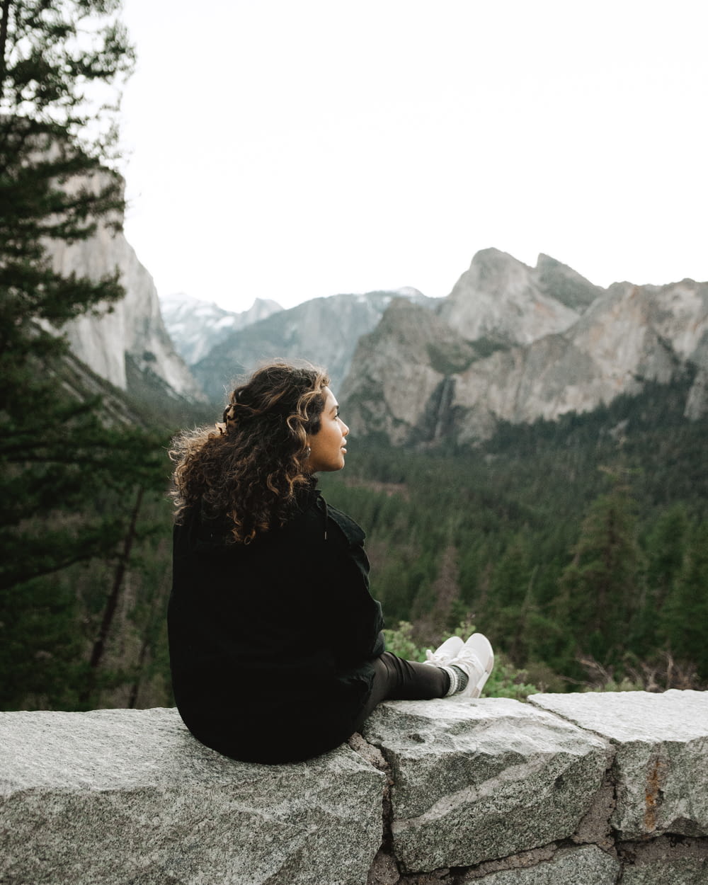 woman in black long sleeve shirt sitting on rock near lake during daytime