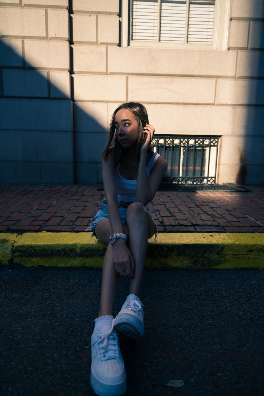 woman in black tank top and blue denim shorts sitting on gray concrete pavement