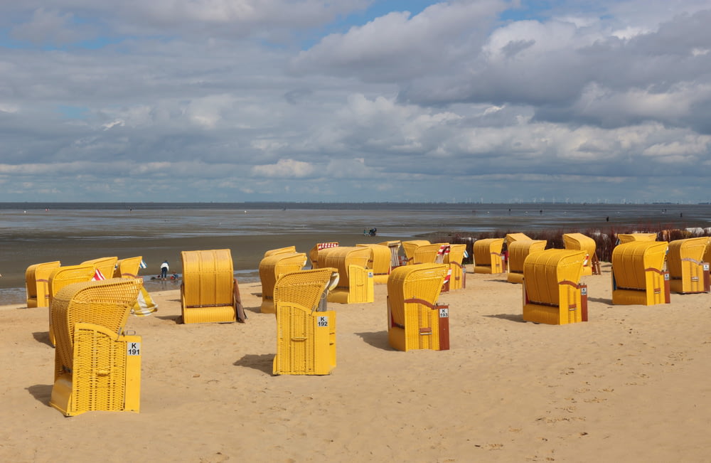 lixeiras plásticas amarelas na areia marrom sob nuvens brancas durante o dia