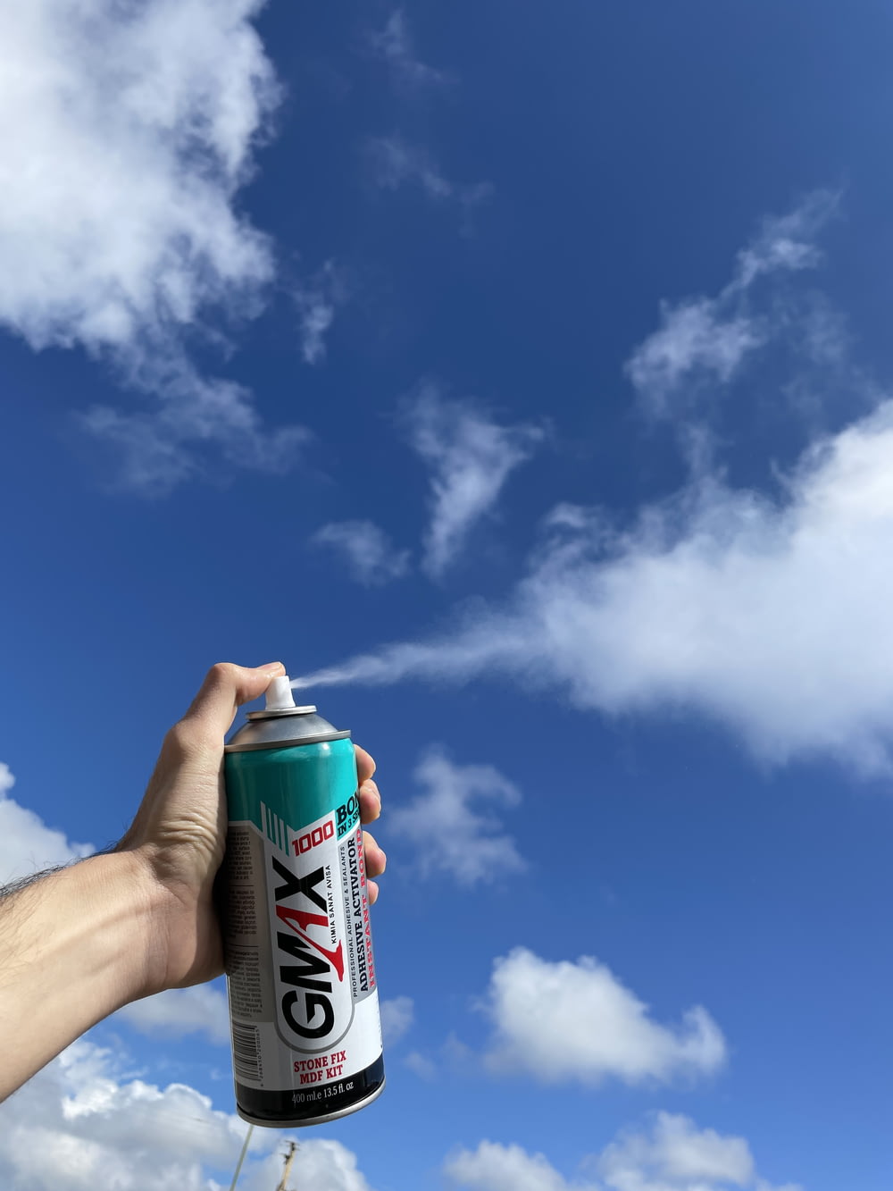昼間、青空と白い雲の下で緑と白のスプレー缶を持っている人