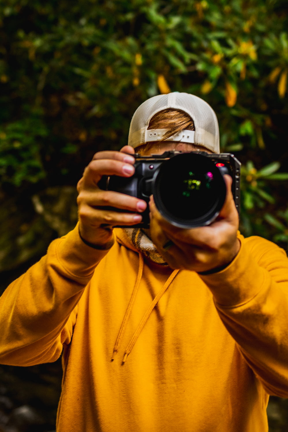 Hombre con sudadera con capucha amarilla tomando fotos con una cámara DSLR negra