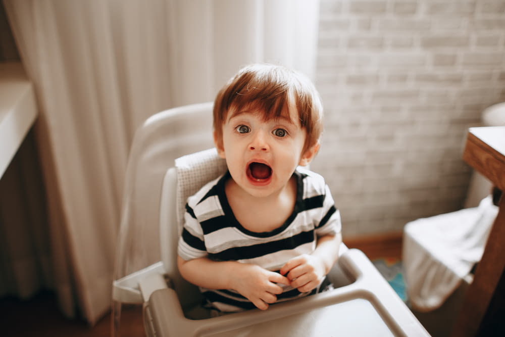 boy in black and white striped shirt sitting on white high chair