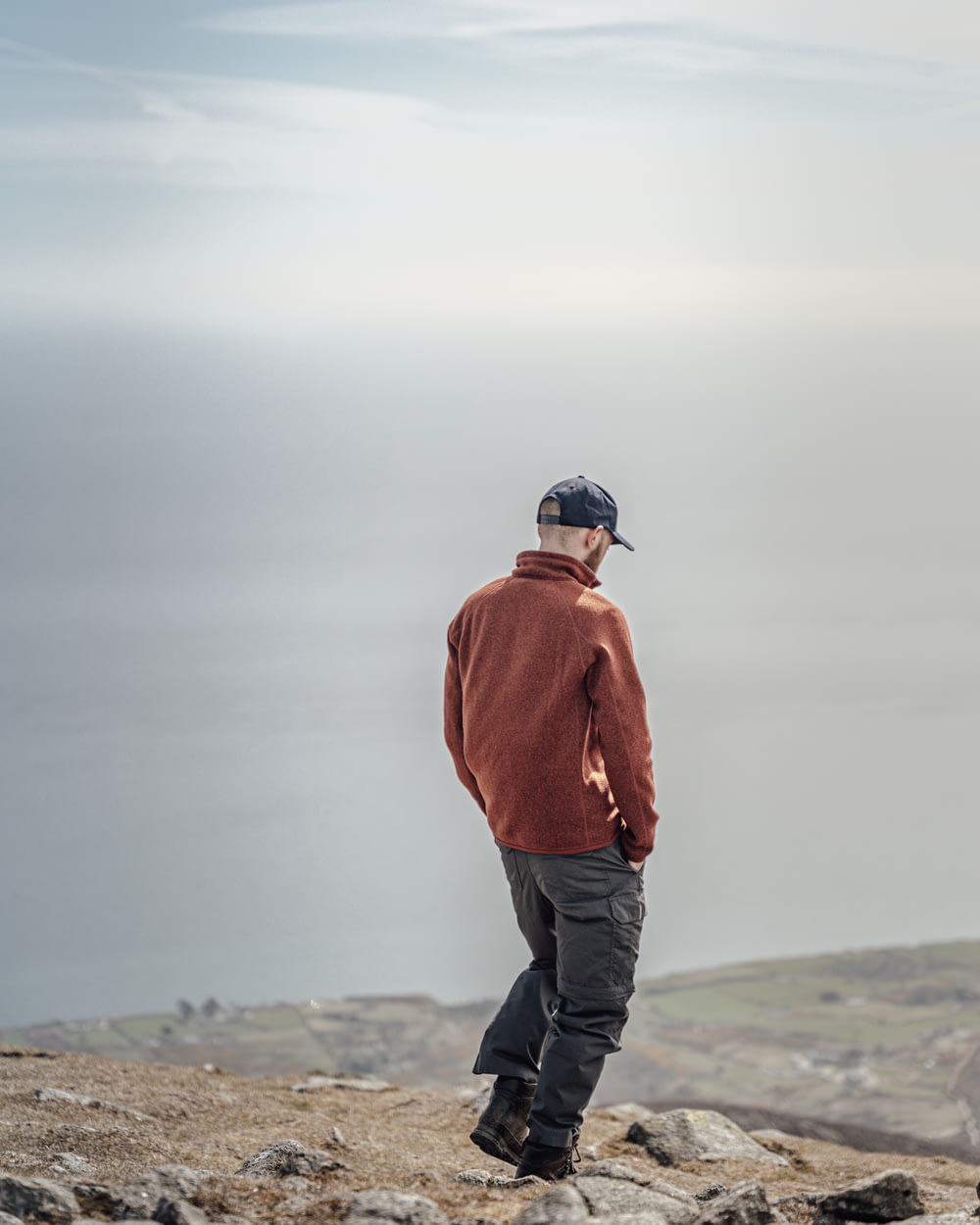 man in orange jacket and black pants standing on gray rock