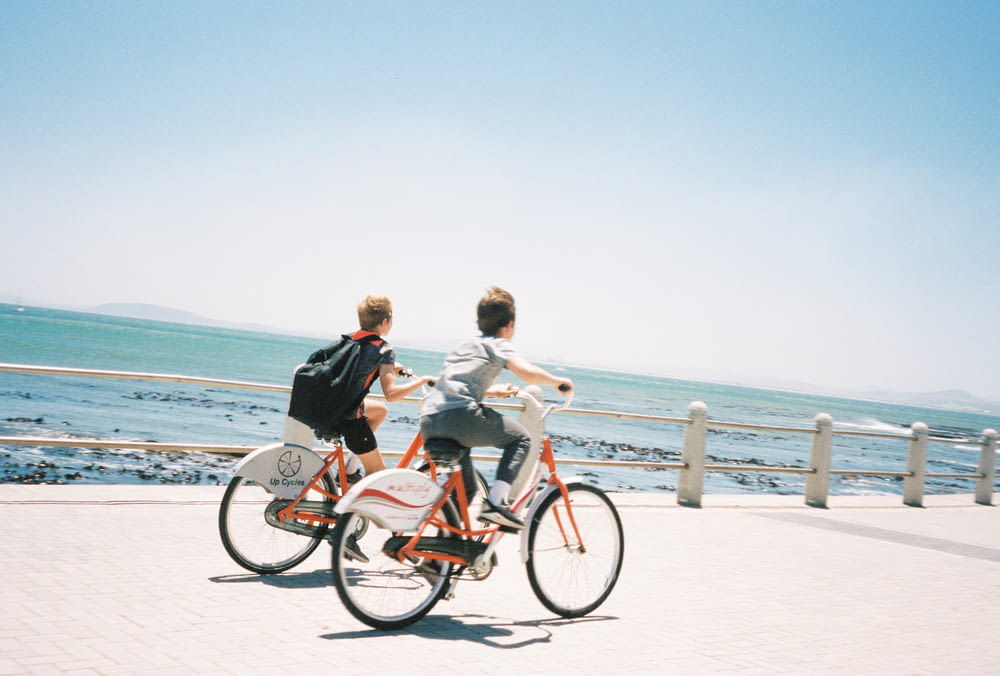 2 mujeres montando en bicicleta roja en playa de arena blanca durante el día