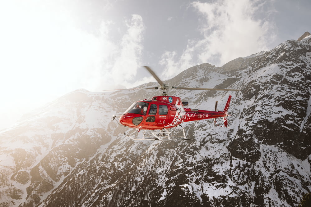 낮에는 눈 덮인 산 위를 비행하는 빨간색과 흰색 헬리콥터