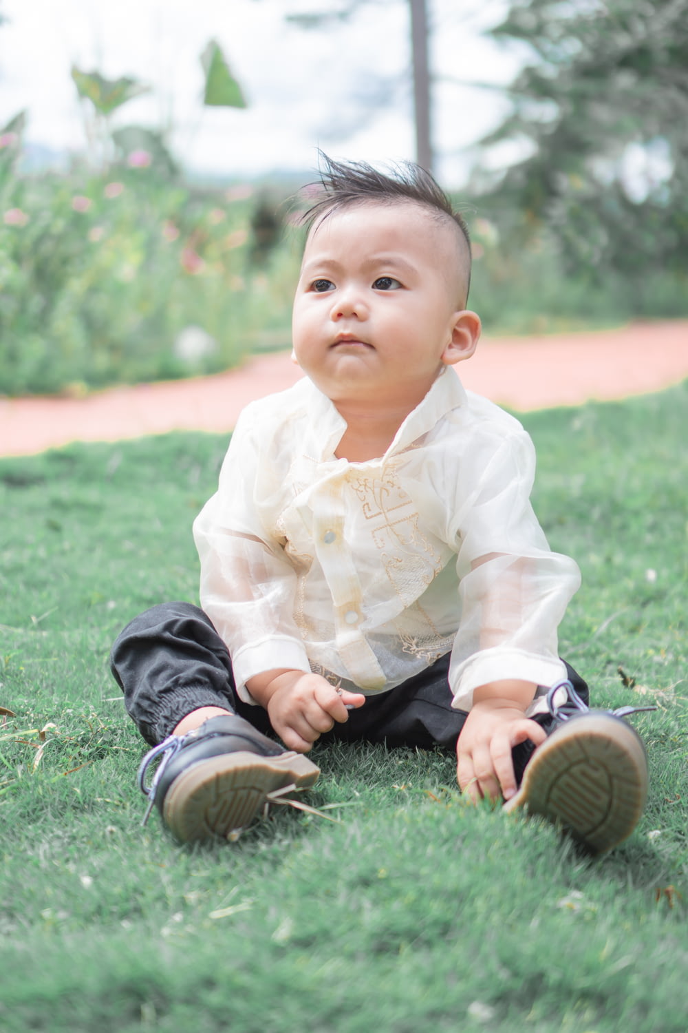 boy in white dress shirt and black pants sitting on green grass field during daytime